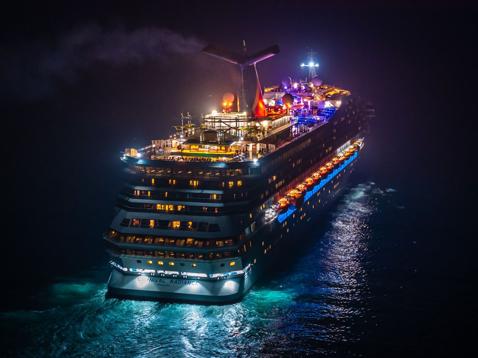 Carnival cruise ship lit up at night with its winged funnel glowing, the line behind every Carnival Cruise Line sale
