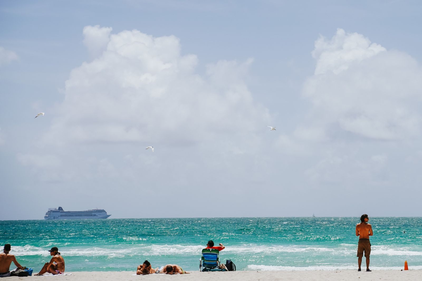 Beachgoers on a turquoise shore with a cruise ship on the horizon, a Celebrity Cruises biggest sale of the year destination