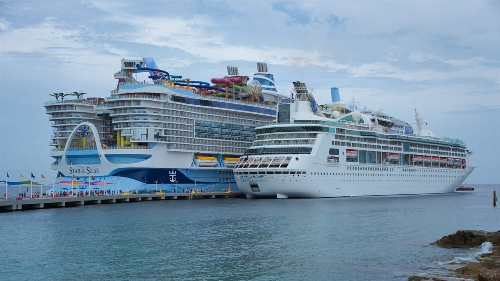 Two large Royal Caribbean cruise ships docked side by side at a sunny island pier